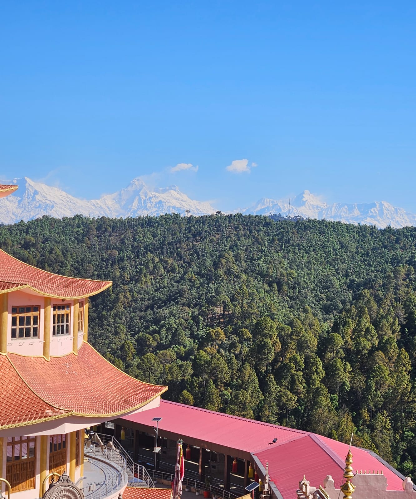 The pagoda temple of Dol Ashram with forested ridges and the Himalayan snow line beyond