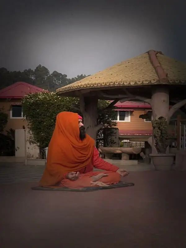 A swami seated in japa practice on the ashram grounds at dusk